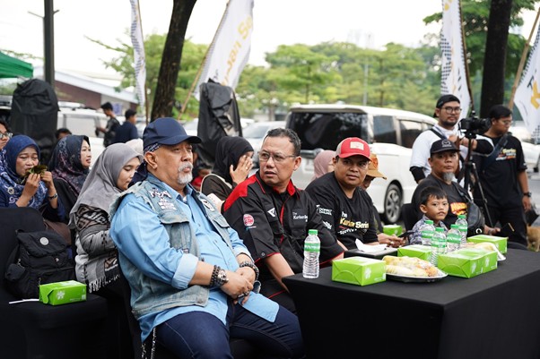 kurbanvala2026indrowarkop2 dompet dhuafa People sitting at a long table outdoors at an event, with boxed meals, bottled water, and snacks; adults and a child present.