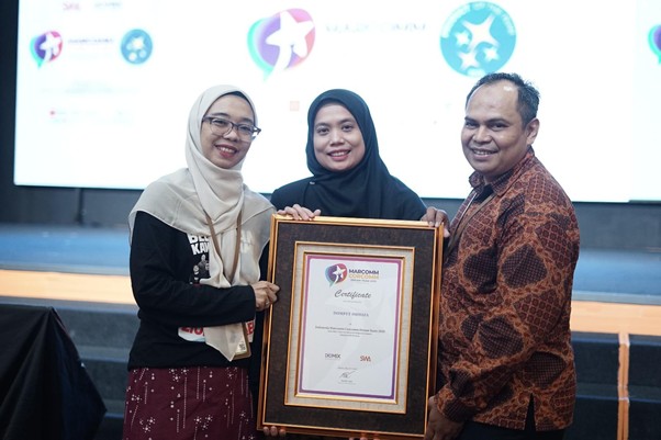 marcomm corcomm dream team 1 dompet dhuafa Three people on a stage holding a framed certificate, smiling for a photo during an award ceremony.