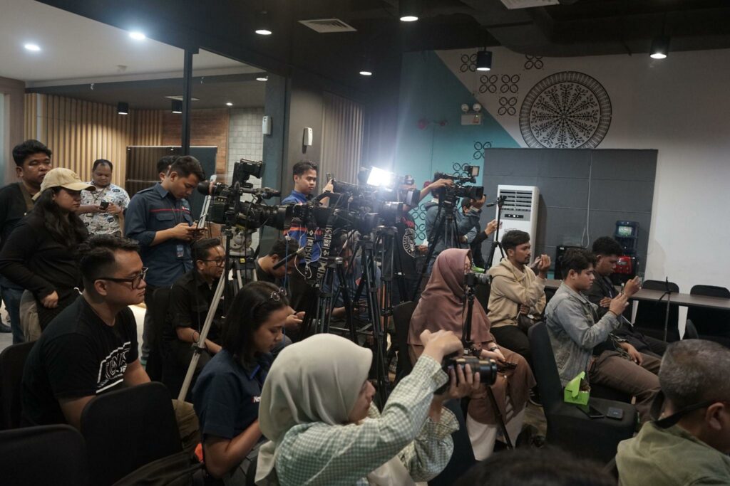 Group of photographers with professional cameras and tripods lined up in a conference room, filming a briefing.