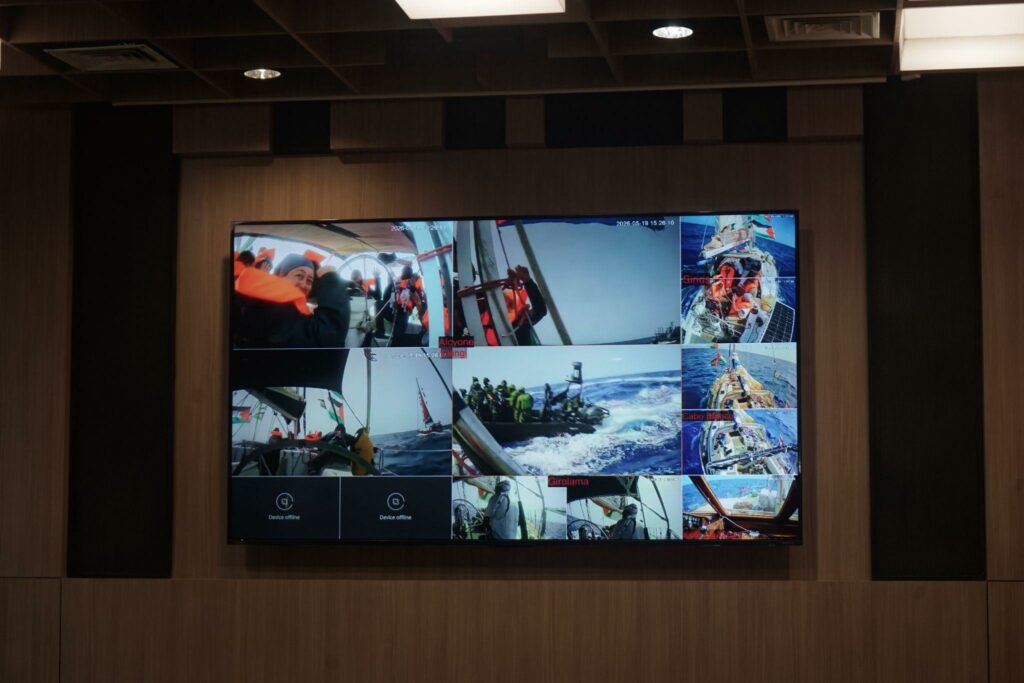 Video wall showing a collage of sailboat photos inside a wood-paneled conference room.