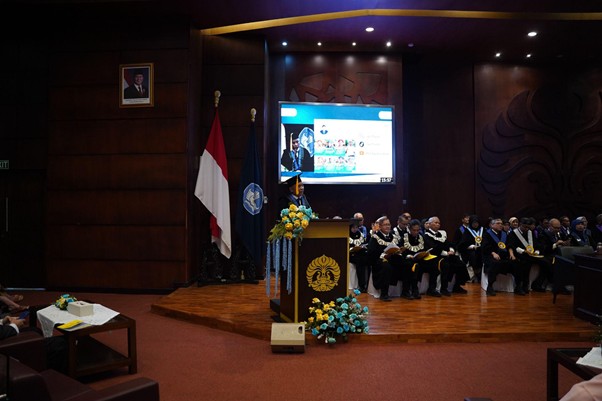 pelantikanagustinozulys6 dompet dhuafa Formal ceremony in a conference hall: speaker at a podium on a stage with flags, floral arrangements, and an audience in regalia beside a large screen.