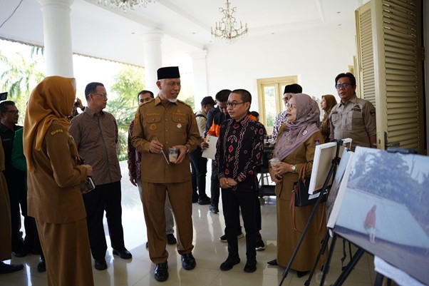 pemprovsumaterabarat12 dompet dhuafa Group of officials in tan uniforms standing in a bright veranda, viewing photographs displayed on easels.