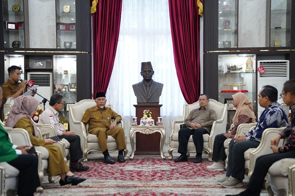 pemprovsumaterabarat2 dompet dhuafa Formal meeting in a government room with a central bust statue on a pedestal, red curtains, and officials seated in two opposing rows.