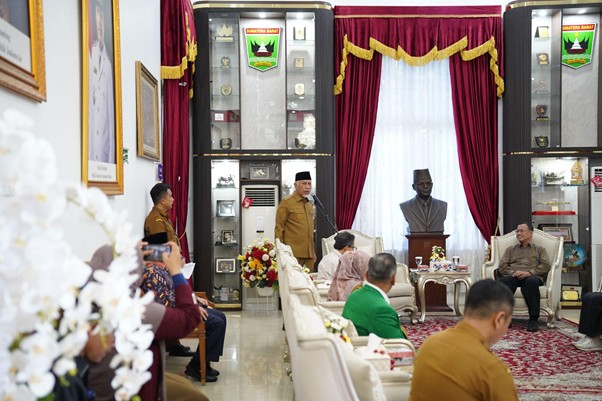 pemprovsumaterabarat4 dompet dhuafa Official meeting in a ceremonial room: uniformed officials sit around a table while a speaker stands at a podium under red curtains and display cases.
