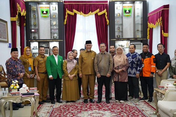 pemprovsumaterabarat9 dompet dhuafa Group of men and women in formal and traditional attire posing for a group photo in a room with red curtains and display cabinets filled with awards or trophies.