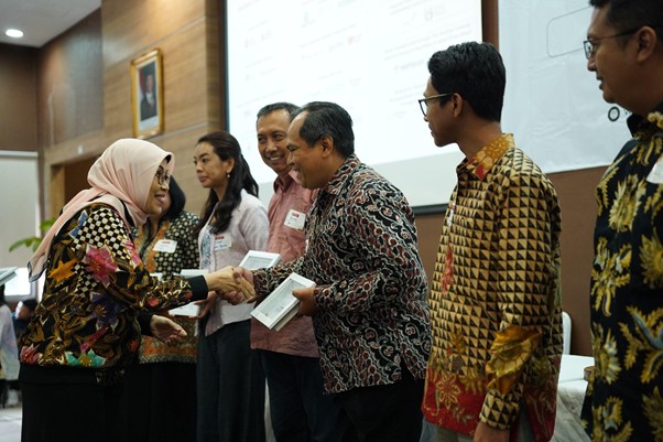 penghargaanpenghimpunanfilantropiindonesia5 dompet dhuafa A woman in a hijab shakes hands with a man and hands him a certificate at a formal ceremony, others waiting in line behind them.