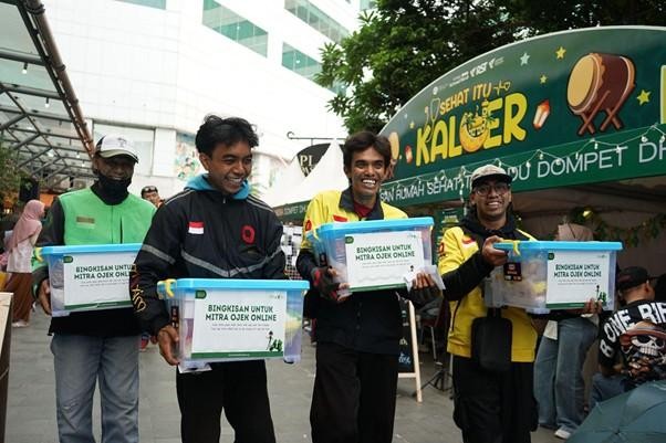 Four men stand outdoors smiling, each holding a donation box labeled for online motorcycle taxi partners at a charity event.