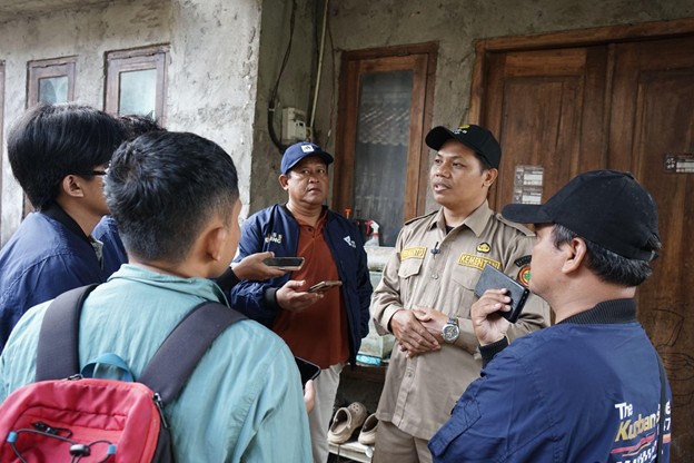 Group of men in uniform standing outside a weathered building, some holding phones and discussing.