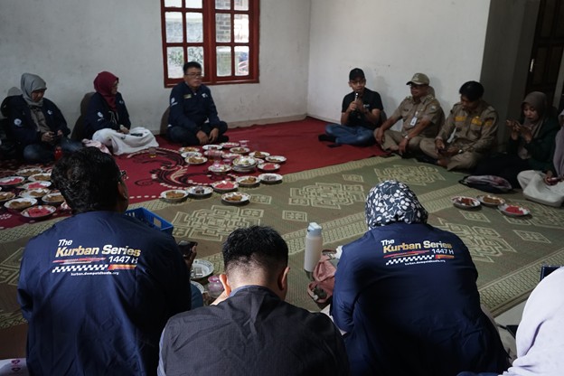 press touring kurban 1447 h 6 dompet dhuafa Group of people sitting in a circle on a rug in a room, sharing a communal meal with bowls arranged in the center; two volunteers in blue jackets labeled'The Kurban Series' face away from the camera.