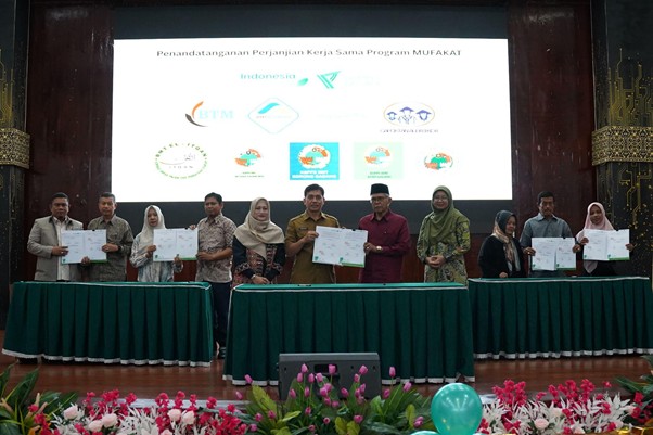 program mufakat 1 dompet dhuafa Group of men and women standing behind green-draped tables on a stage, each holding a certificate during a formal signing ceremony, with a large screen displaying logos and Indonesian text in the background.