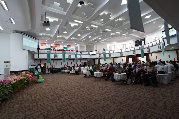 programmufakat2 dompet dhuafa Audience seated in a large conference hall facing a projector screen and stage on the left. Colorful banners hang from the balcony around the room.