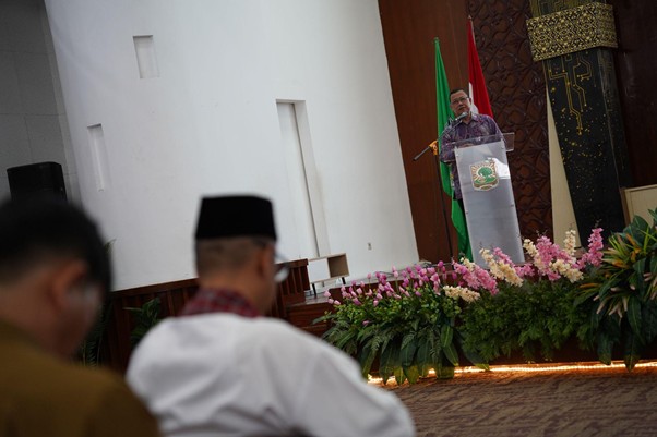 programmufakat4 dompet dhuafa Speaker delivers a speech at a podium on a stage, with green and red flags and a floral arrangement in front.
