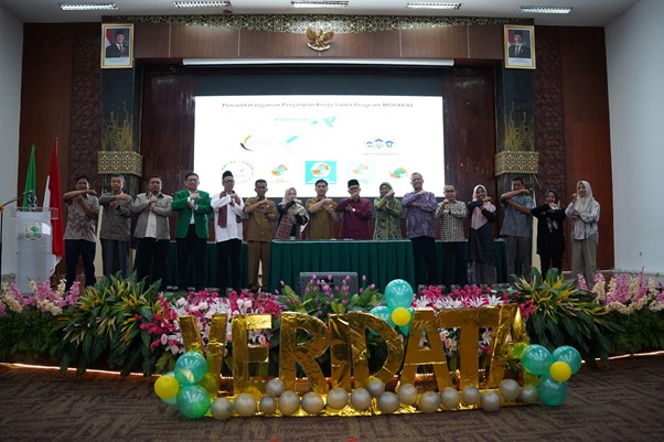 programmufakat8 dompet dhuafa Group of people on a decorated stage posing for a photo, with a projector screen behind them and balloons and flowers at the front.