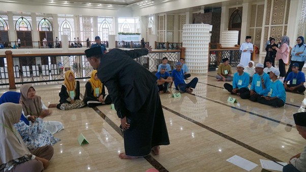 Teacher in black robes leads a discussion as students sit in a circle on a shiny floor inside a mosque hall.
