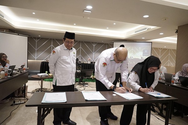 sklaz20263 dompet dhuafa Two people in white uniforms sign documents at a table in a conference room, while a man stands nearby as others observe.