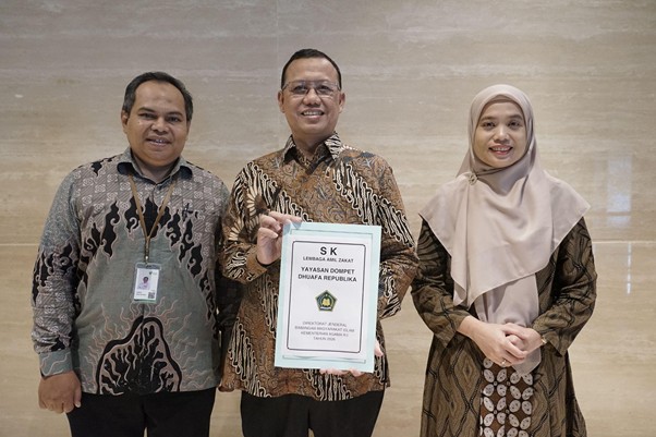 sklaz20267 dompet dhuafa Three people in batik shirts stand together; the man in the center holds a framed certificate.