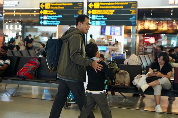 sosok ronggo dan herman 6 dompet dhuafa Man with a backpack walks with a child through an airport terminal, signs and passengers in the background.