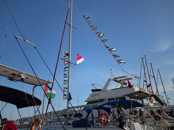 Sailboats docked at a marina with colorful pennant flags fluttering in a clear blue sky.