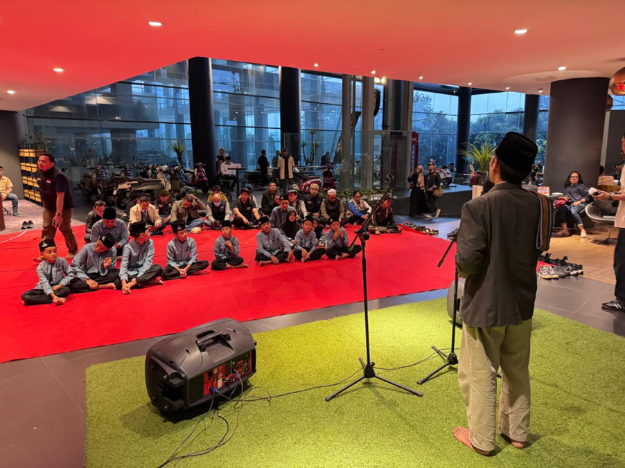 vespa60sjabodetabekdanscomadiindonesia2 dompet dhuafa Group of children seated on a red carpet indoors, watching a musician in traditional clothing with a guitar near a microphone and speakers in use.