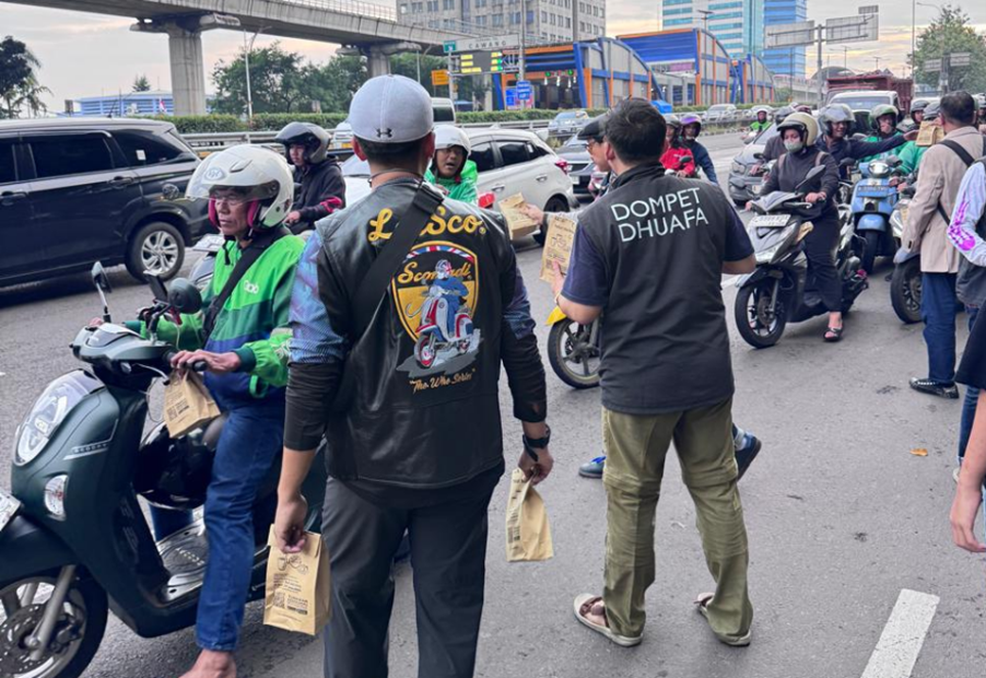 vespa60sjabodetabekdanscomadiindonesia4 dompet dhuafa Group of motorcyclists lined up on a city road receiving paper bags from volunteers during a charity event; one man wears a 'Dompet Dhuafa' shirt.