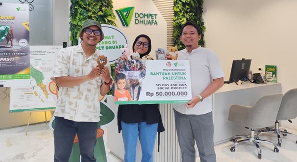 Three people stand in a bright lobby, holding a large donation check reading Bantuan Untuk Palestina for Rp 50,000,000, with Dompet Dhuafa branding in the background.