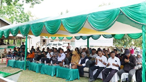 perkuatnelayandisumatra2 dompet dhuafa Outdoor community gathering under a green canopy with long row of seated attendees, many with hands raised in prayer or praise.