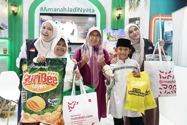 Group of five people (four women in hijabs and a boy) smiling at a colorful booth, each holding shopping bags for a photo.