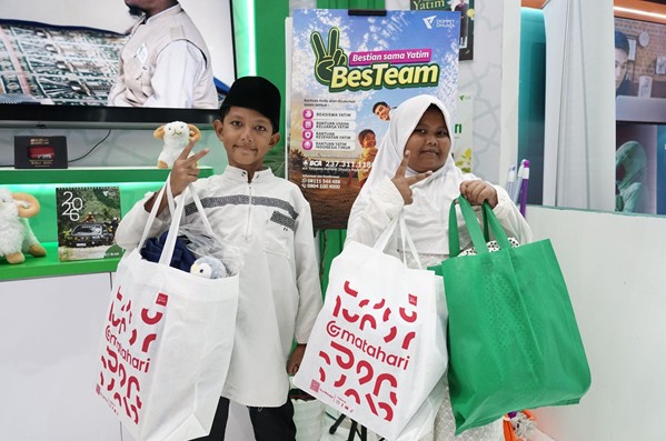 Two kids wearing white traditional clothes pose with white and green reusable bags at a booth featuring a Besteam sign.