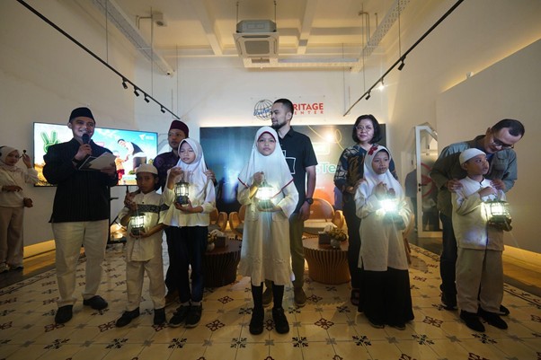 Group of children in white outfits holding lanterns, with adults behind, at an indoor heritage event in a gallery.