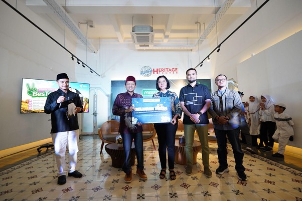 Six people pose with a large ceremonial check in a bright room, Heritage branding visible on the wall behind them.