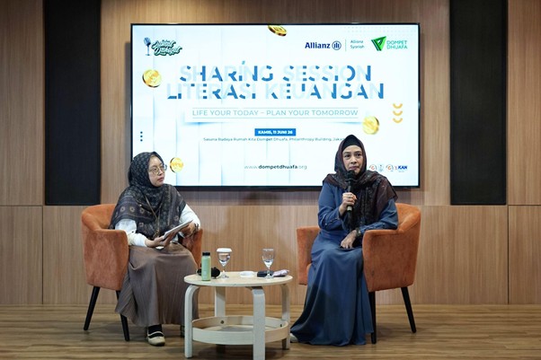 Two women in hijabs seated on orange chairs during a panel discussion, with a small table of drinks between them; a large screen behind shows the event title.