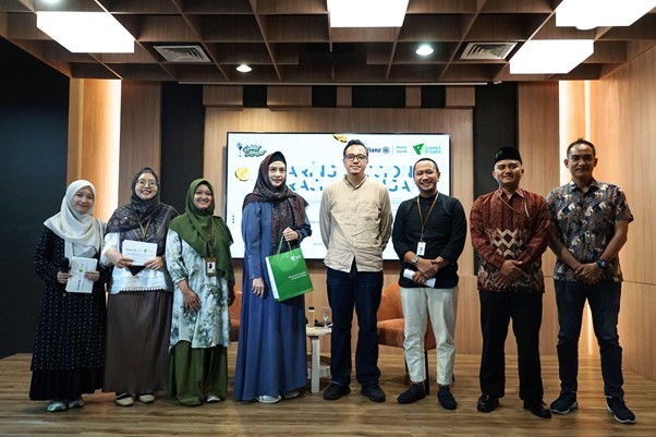 Nine people pose in a line on a stage in a wood-paneled room; several hold certificates and a green folder, with a logo banner on a screen behind them.