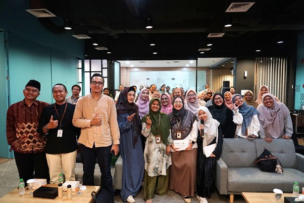 Diverse group of coworkers posing for a group photo in a modern office lounge, some wearing hijabs and lanyards, a certificate visible in the center.