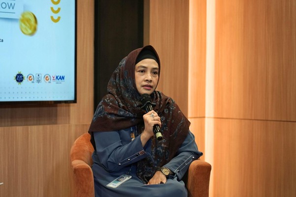 Woman in a hijab sits on an orange chair, speaking into a handheld microphone during a panel discussion.