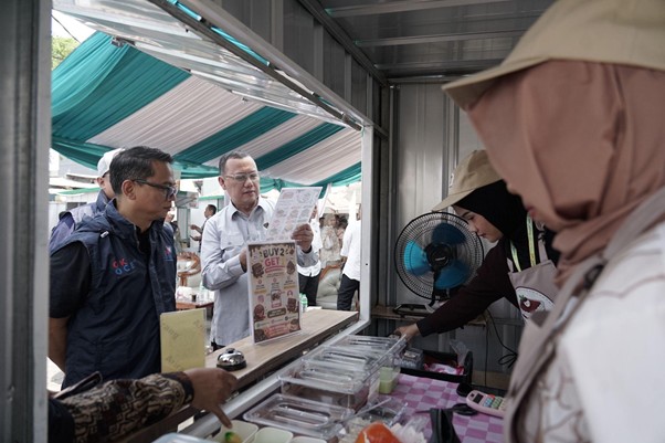 foodcourt nusadaya bogor 9 dompet dhuafa Man in a white shirt shows a menu to two customers at a street food stall under teal and white canopy.