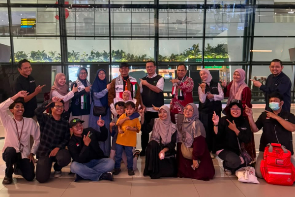 fotojet 3 dompet dhuafa Group of about 20 people posing for a group photo in an airport terminal, many smiling and giving thumbs up, plus a child at centerfans/ A diverse crowd in casual clothing.