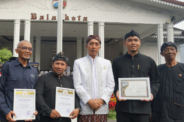 fotojet dompet dhuafa Five men stand in front of a white, columned building, holding framed certificates; center man wears a white traditional jacket for an award ceremony.