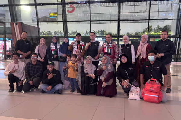 fotojet dompet dhuafa Group of people posing for a photo in an airport terminal with large windows behind them. They include adults and a small child, some wearing hijabs and masks.