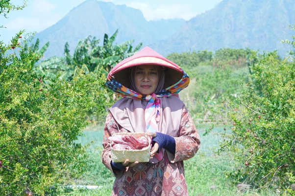 iduladha di rumah bu zahroh 1 dompet dhuafa Woman in a conical hat stands among greenery, holding a woven basket in a fruit grove with mountains in the background.