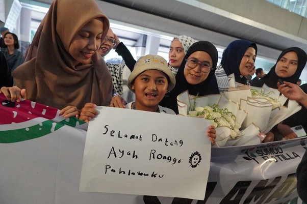 kedatangandelegasigsf202 dompet dhuafa Child in a white hat holds a sign reading 'Selamat Datang' while smiling women with bouquets surround and welcome him at a ceremony.