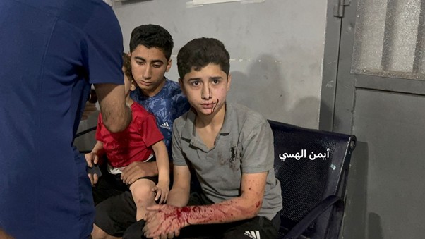Two injured boys sit in a clinic while a healthcare worker tends to them.