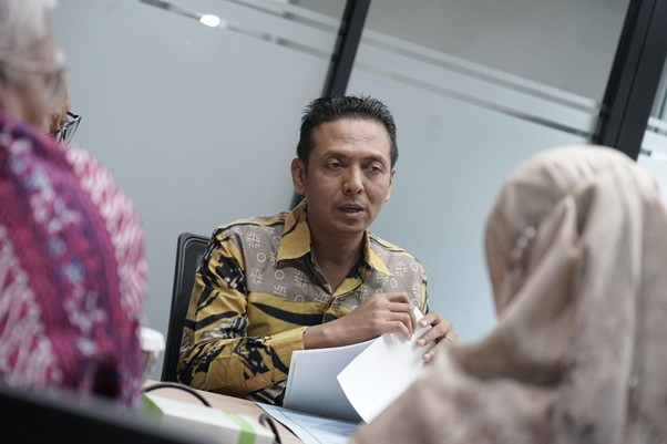 Man in a patterned shirt explains documents during a meeting with two coworkers.