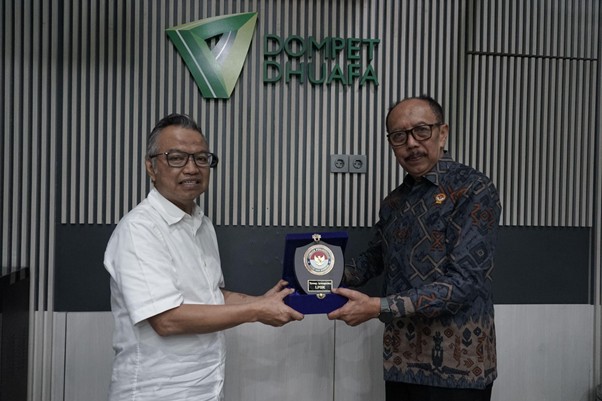 Two men shake hands while presenting a blue award plaque in front of a wall featuring the Dompet Dhuafa logo.