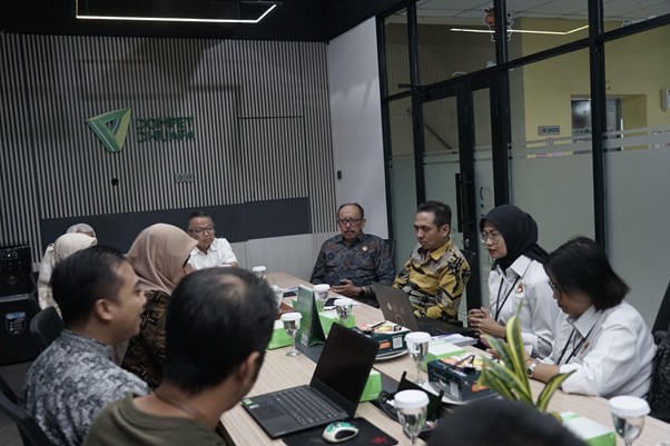 Diverse team in a modern conference room around a long table with laptops and coffee during a meeting.