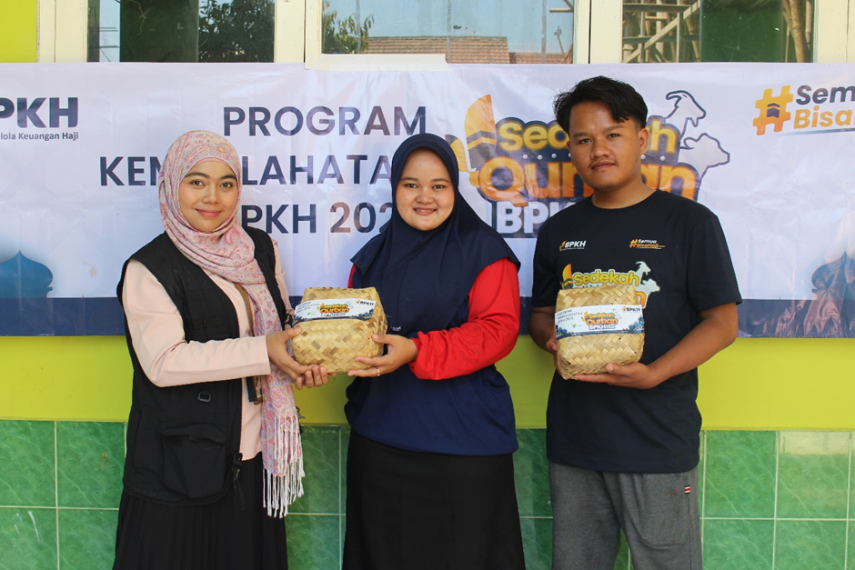kurban bpkh 4 dompet dhuafa Three people stand in front of a banner for a health program, each holding a woven gift basket (two women and one man). They pose for a photo at the event.