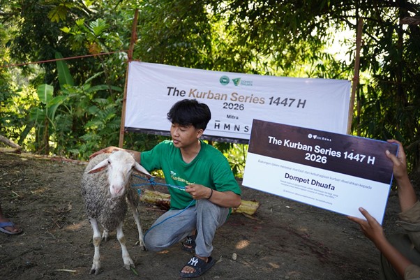 Man in a green shirt kneels beside a sheep outdoors, holding a banner that reads 'The Kurban Series 1447 H 2026'.