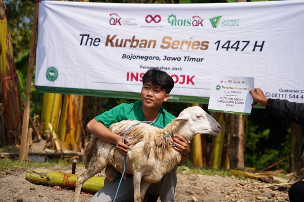 kurbanroisojk4 dompet dhuafa Boy in a green shirt holding a sheep in front of a banner that reads 'Kurban Series 1447 H' at a Bojonegoro, East Java event.