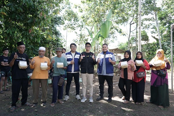 Group of people outdoors showing packaged food aid or donations, standing in a line with trees in the background, some giving thumbs up.