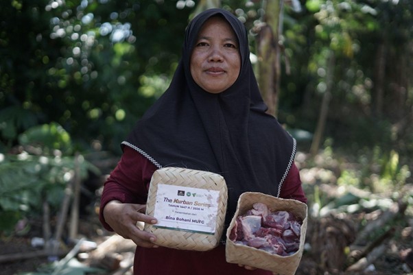 kurban di lampung timur 7 dompet dhuafa Woman in a black hijab and burgundy dress holds two woven baskets of meat, one labeled Kurban Series for a charity drive.