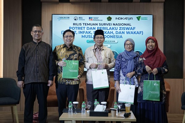 Five individuals stand in a row holding gift bags at a formal event, with a conference banner in the background.